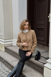 a lady in a white mock neck sweater, a brown wool jacket and a pair of black pants